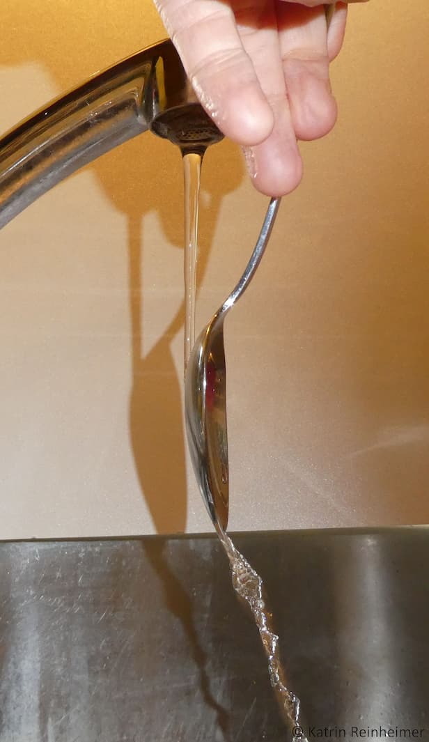 Halte den Löffel wie auf dem Foto in den Wasserstrahl Halte den Löffel wie auf dem Foto in den Wasserstrahl