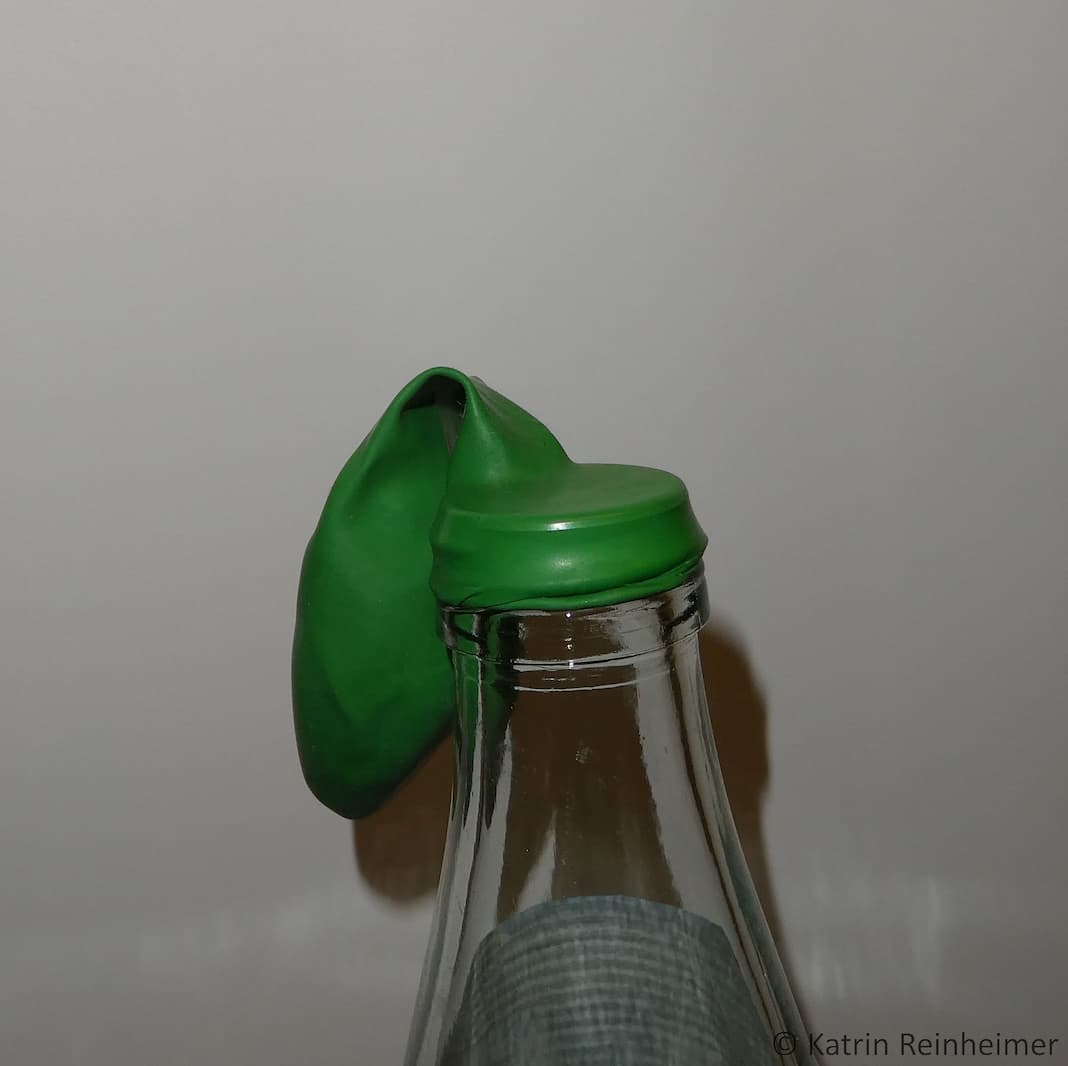 Zieh den Zipfel des Luftballons über die Öffnung der Glasflasche.